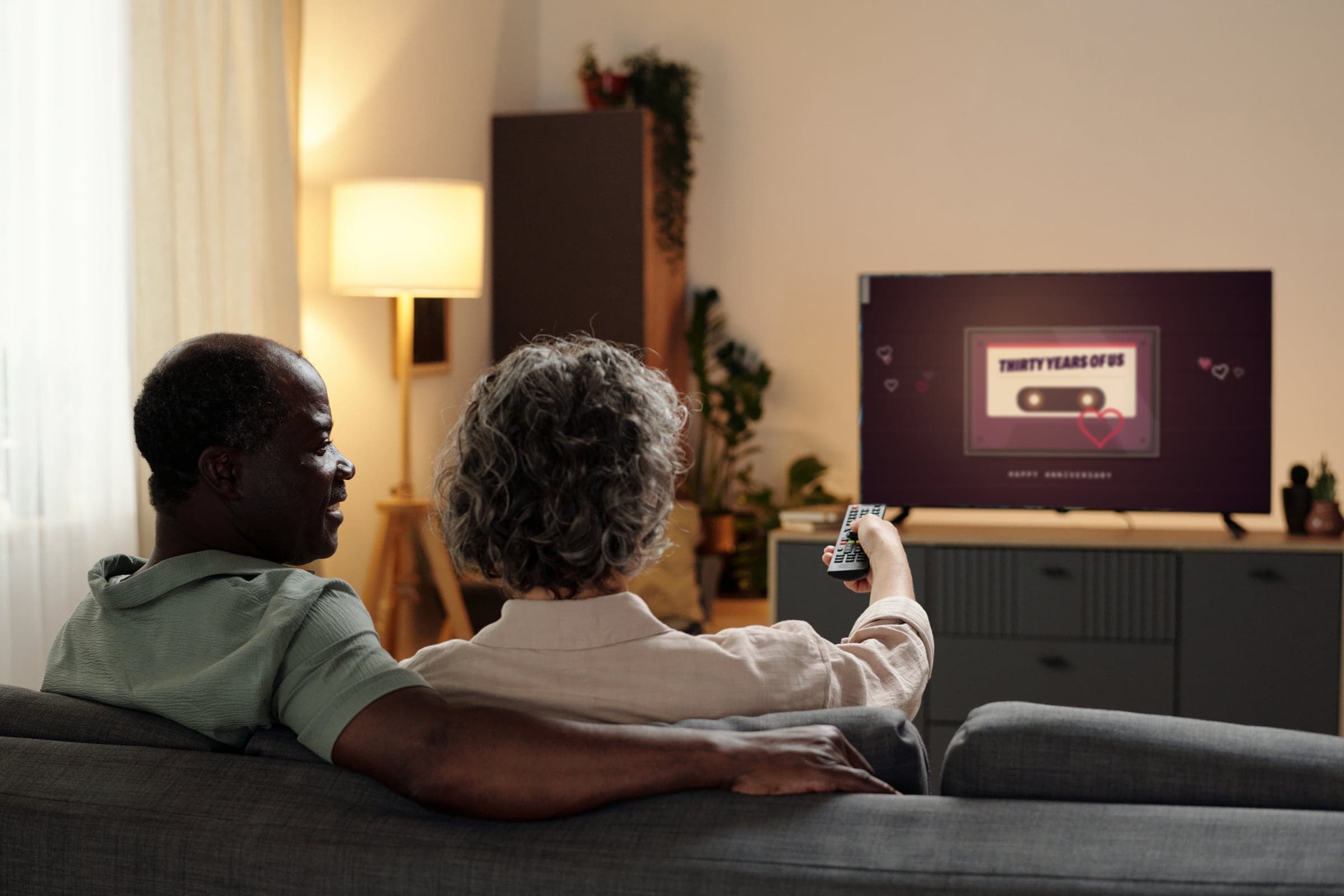 An older couple on the couch watching a tape called Thirty Years of Us on their TV
